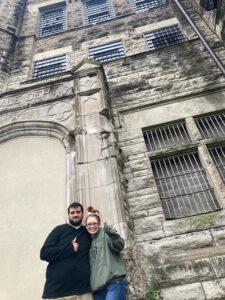 Two people giving thumbs up in front of historic building. Low perspective.