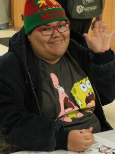 Person at craft table smiling at camera with Holiday hat on.