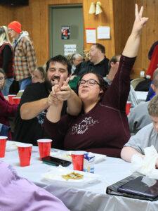 Man and woman at table giving peace sign and laughing.