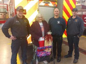 Woman at fire poses with firefighters and fire trucks.