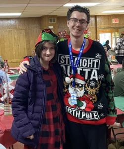 Two people in Christmas sweaters with arms around each other.