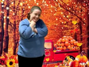 Lady smiling in front of fall background with old truck and pumpkins.