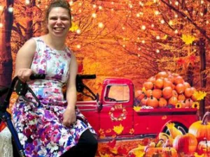 Lady smiling in front of fall background with old truck and pumpkins.