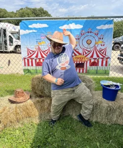 Man in cowboy hat posing in front of hay bales.