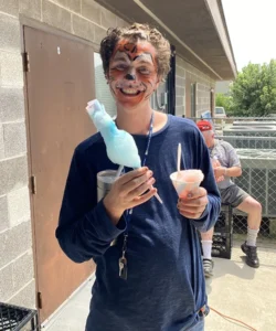 Person smiling with cotton candy, ice shavings, and a painted face.